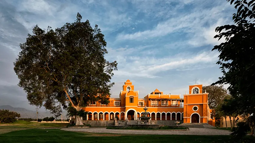 Elegante fachada colonial de la Hacienda Caravedo rodeada de áreas verdes bajo un cielo soleado.