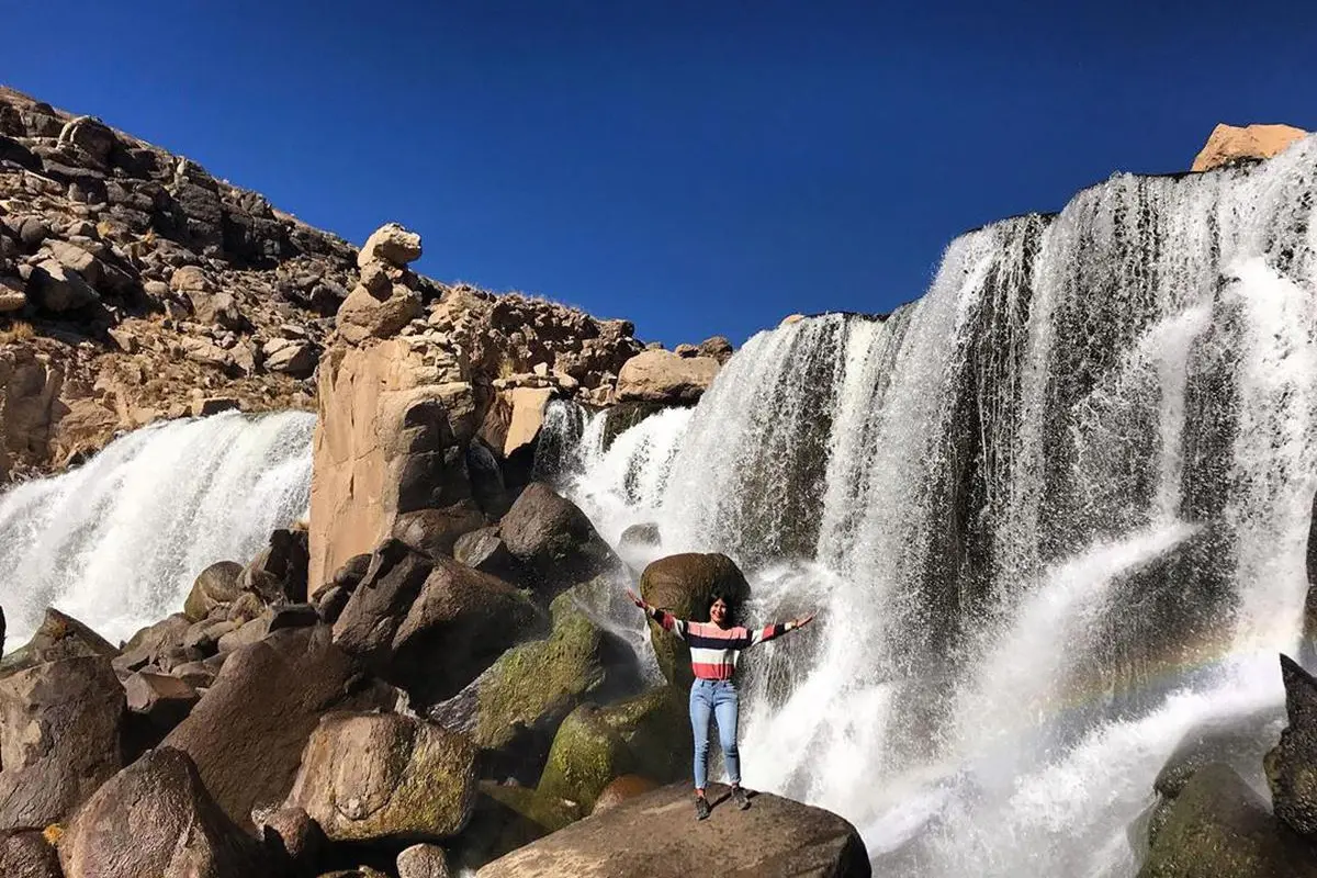 Una viajera posa sonriente con la Catarata de Pillones de fondo durante su recorrido por Arequipa.