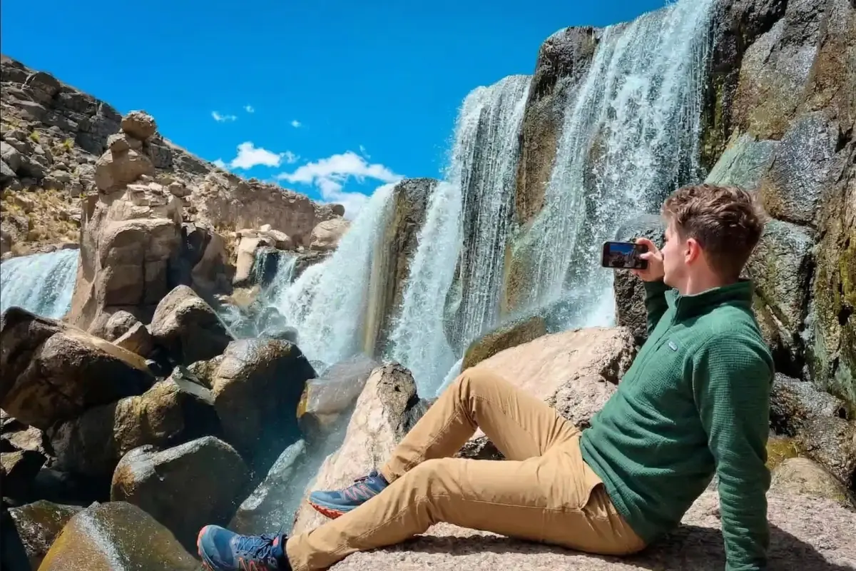 Un turista sentado de espaldas admirando la caída de agua y el paisaje rocoso de Pillones.